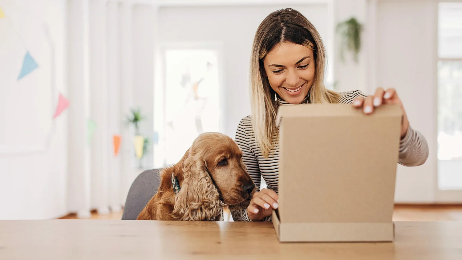 Frau mit geöffnetem Versandkarton und Hund als Bildbeispiel für den Versand